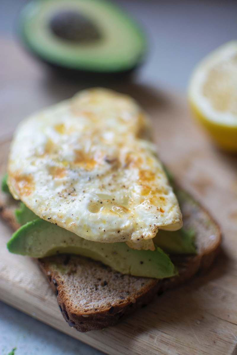 egg egg on top of avocado and bread on chopping board burger