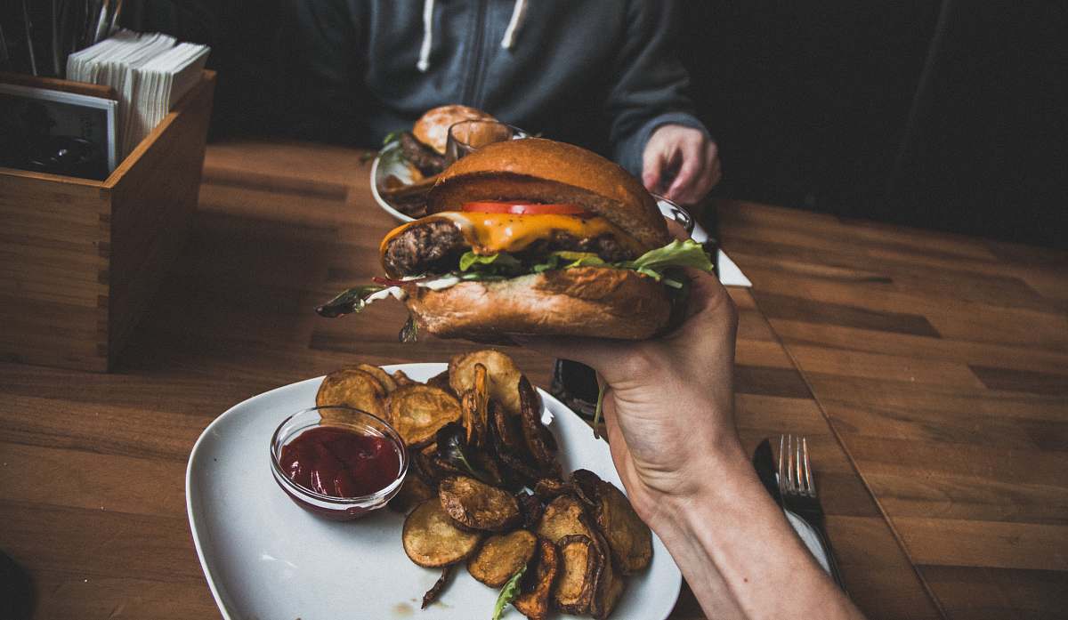 burger person holding burger filled with sliced tomato and lettuce vienna