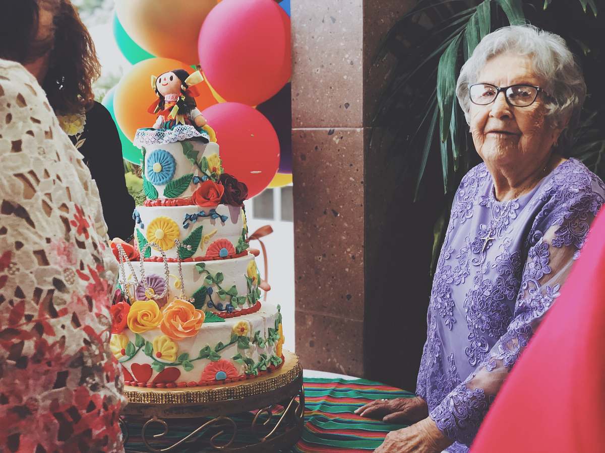 dessert woman wearing purple floral long-sleeved dress besides 4-layer cake cake