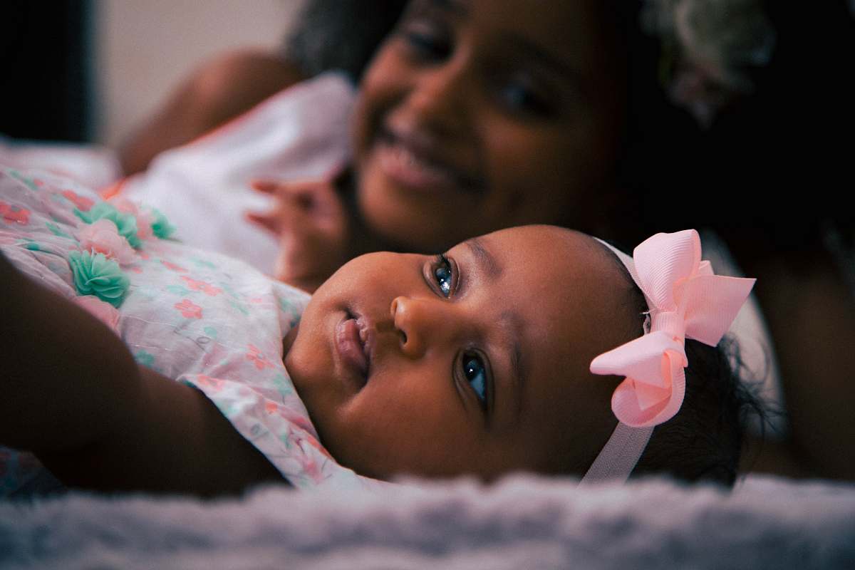 person toddler wearing white and pink headdress lying near girl baby