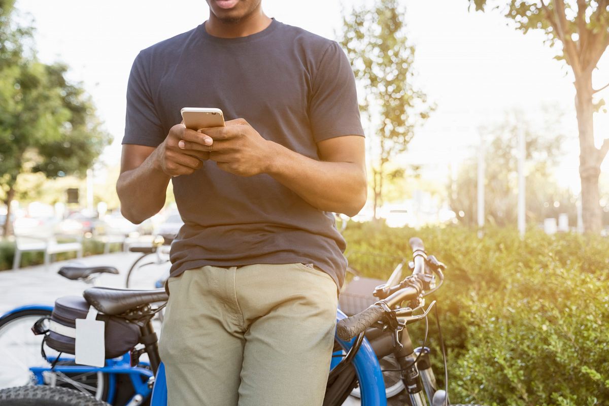 man holding smartphone leaning on bicycle during daytime