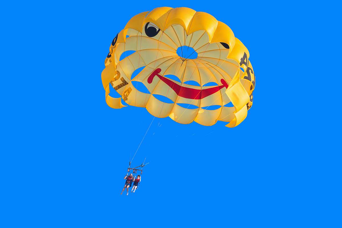 adventure two person in yellow, red, and black parachute under blue sky during daytime leisure activities