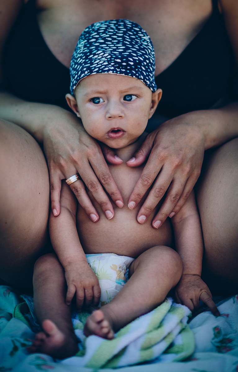 baby baby wearing white and black cap near woman wearing black bra people
