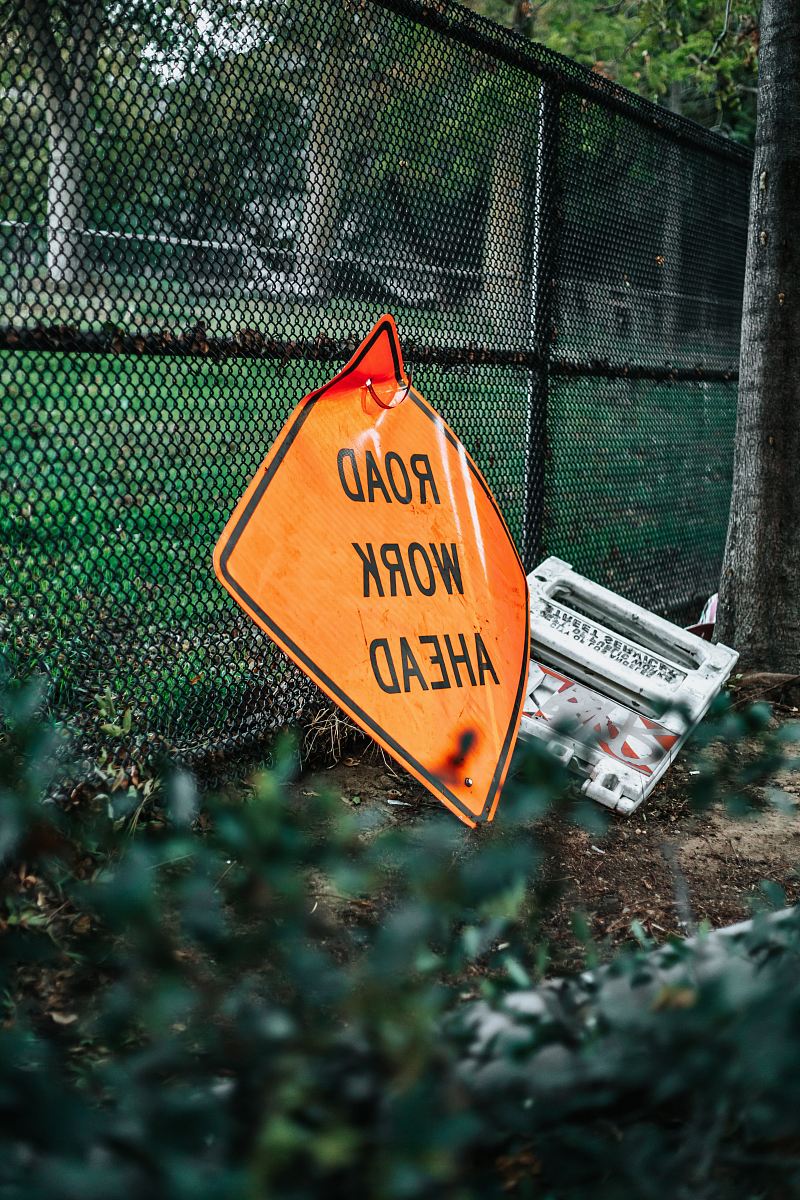 road work ahead signage leaning on chain link fence