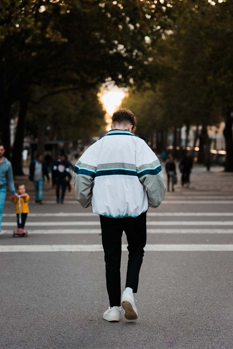 tarmac man wearing white and blue jacket and black jeans walking on street road