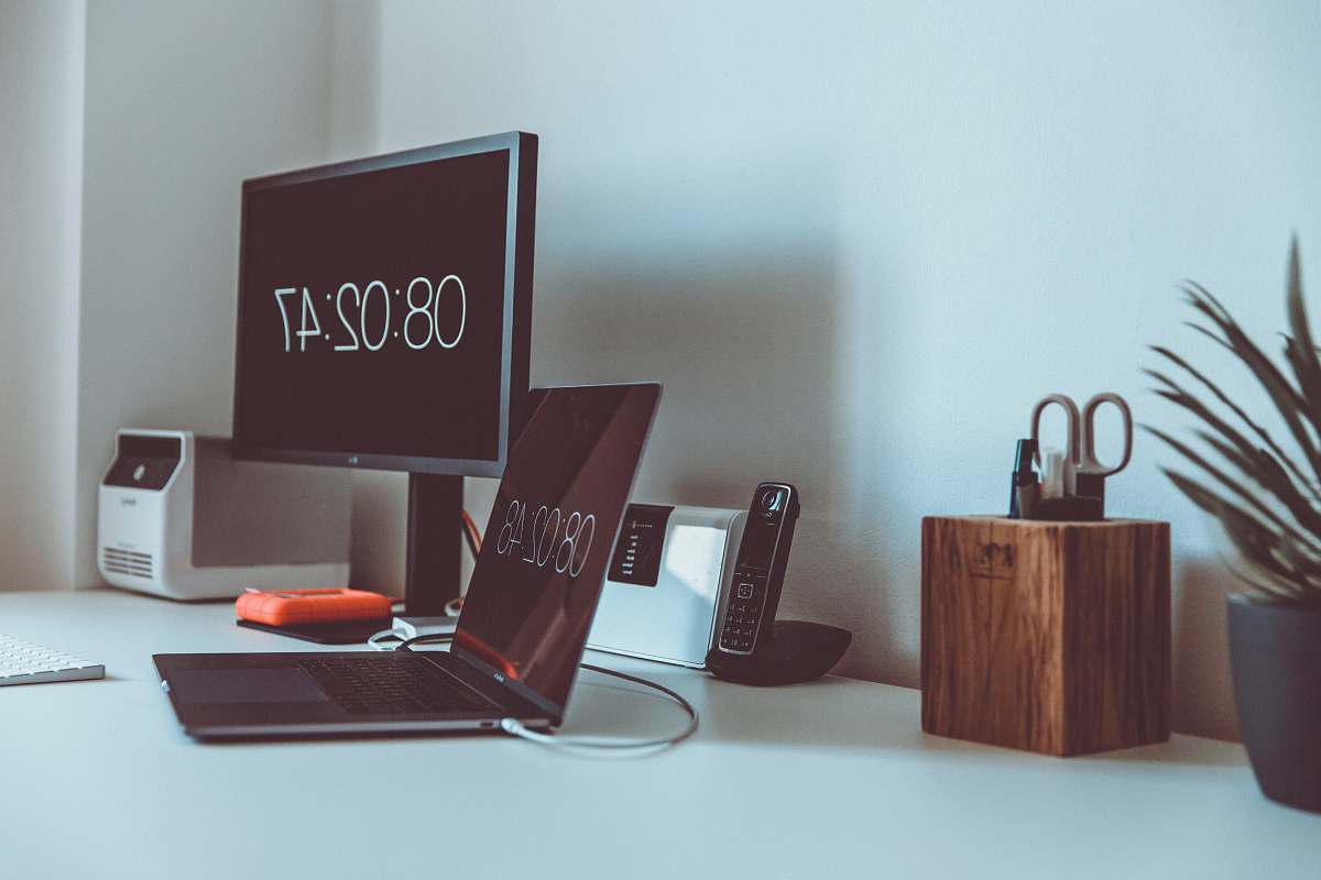 plant turned on computer monitor and laptop with 08:02:47 on screens desk