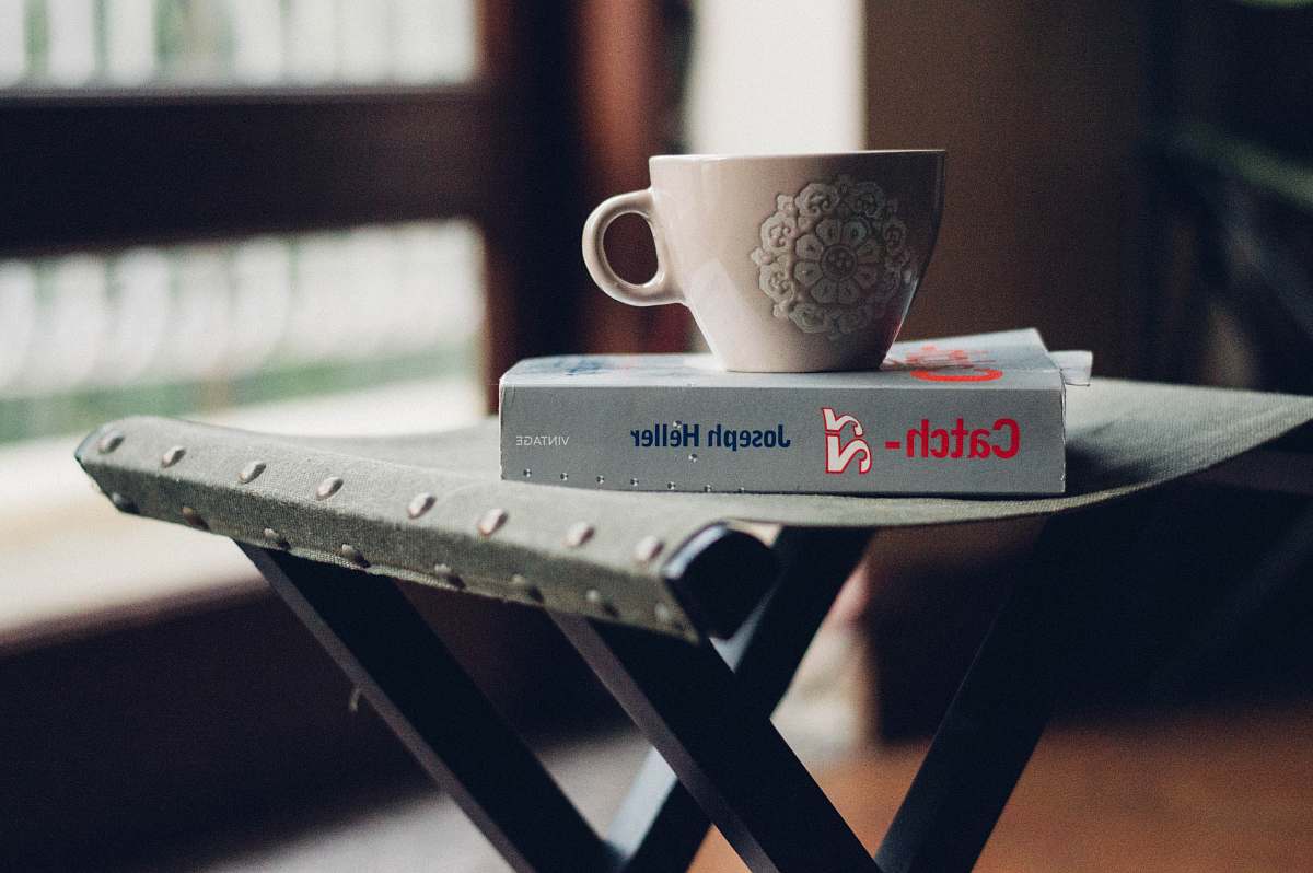 furniture close-up photography of beige ceramic coffee cup on top of Joseph Heller book table