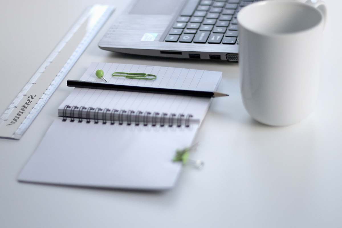office black pencil on ruled notepad beside white ceramic mug and gray laptop computer work