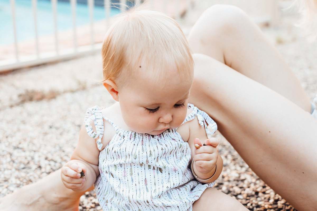 person baby sitting on sandy ground while holding pebbles people