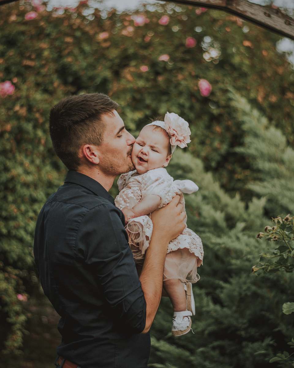 person men holding a baby near plants during daytime clothing
