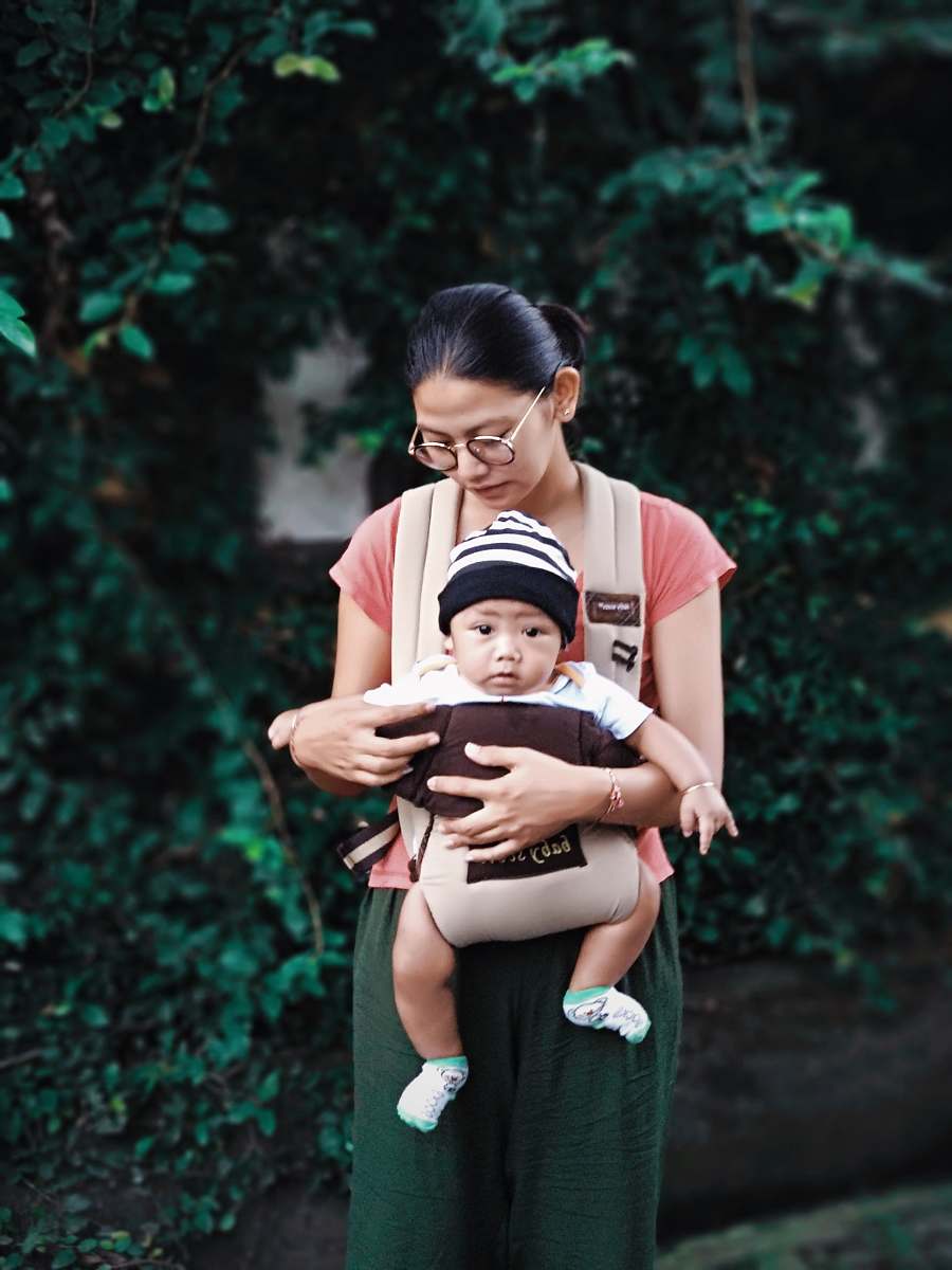 person woman holding baby beside green plants apparel