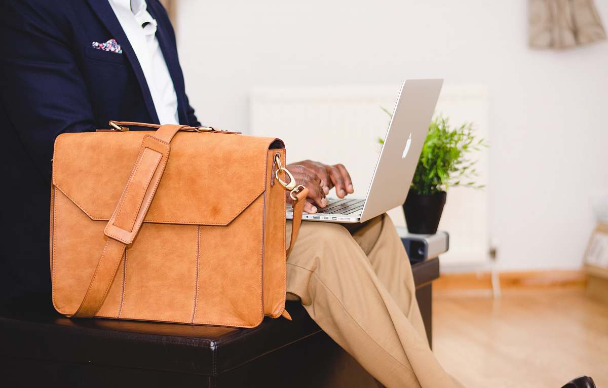work person using MacBook Pro beside brown leather briefcase business