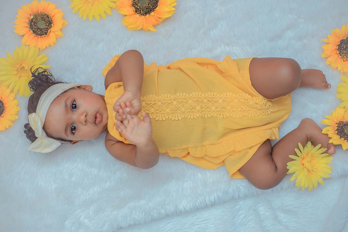 human baby in yellow dress lying on white textile diaper