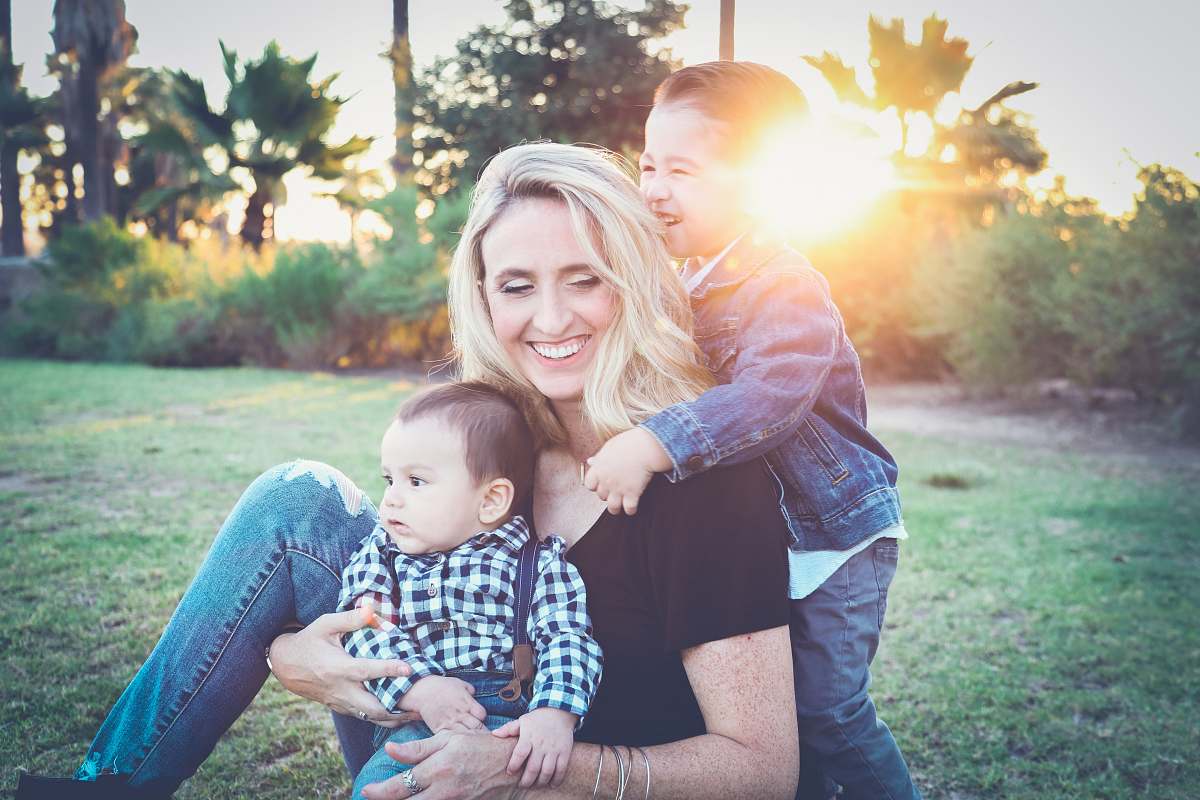 family woman holding baby sitting on green grass field under sunset woman