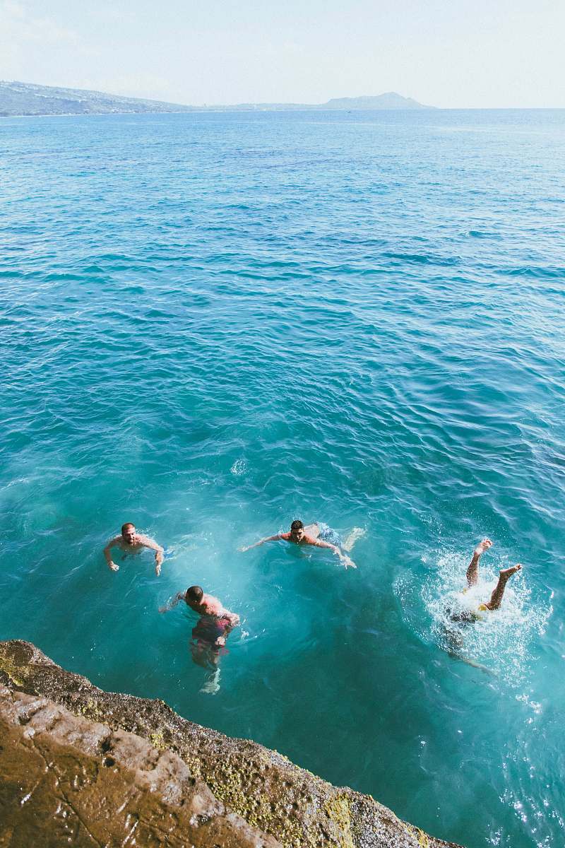 water aerial photography of four men swimming in blue sea human