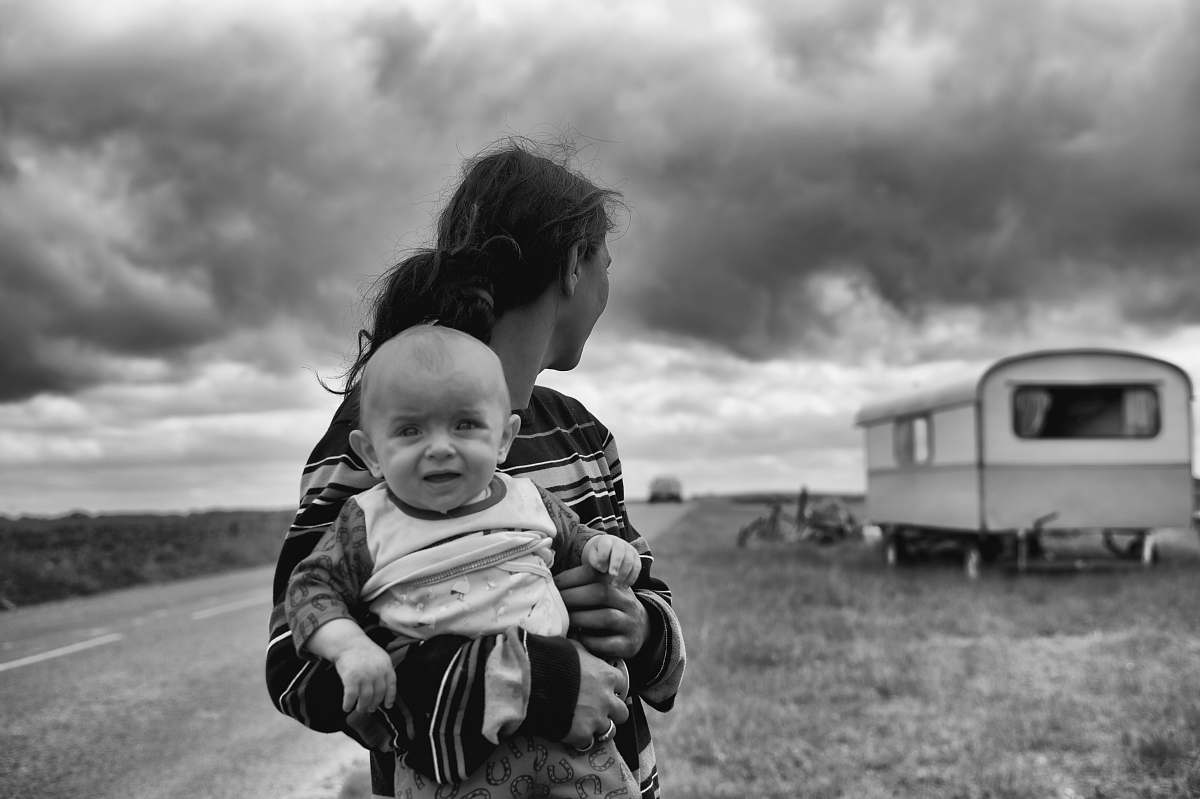 black-and-white gray scale photography of woman carrying baby looking at camper trailer people
