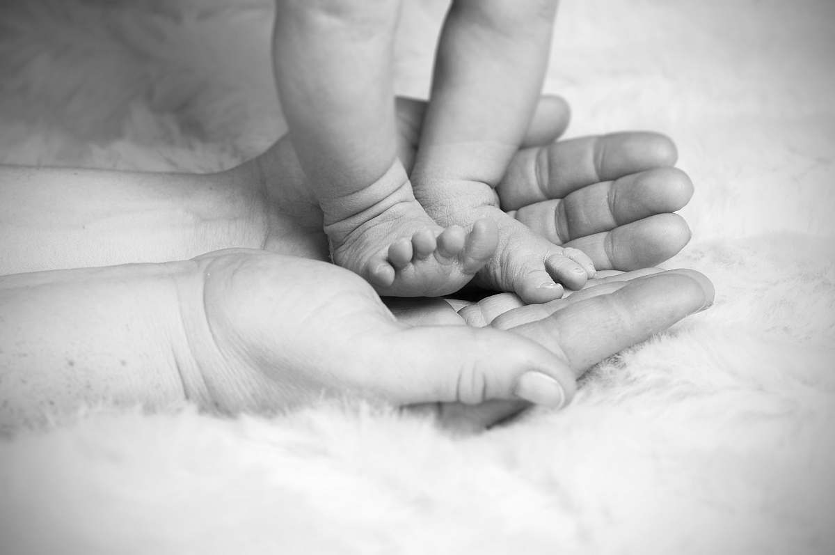 black-and-white grayscale photo of baby's foot on human palm hand