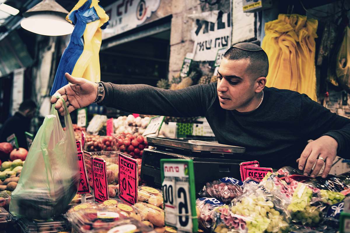 human man reaching out with green plastic bag on hand over assorted fruits display market