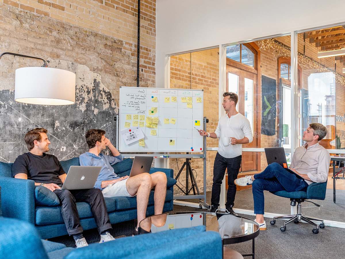 sitting three men sitting while using laptops and watching man beside whiteboard human