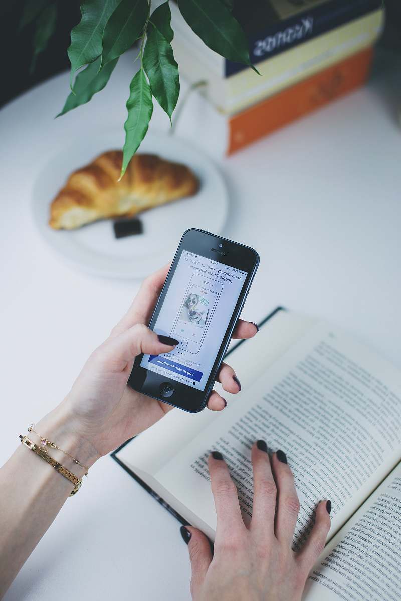 book person using phone in front of open book croissant
