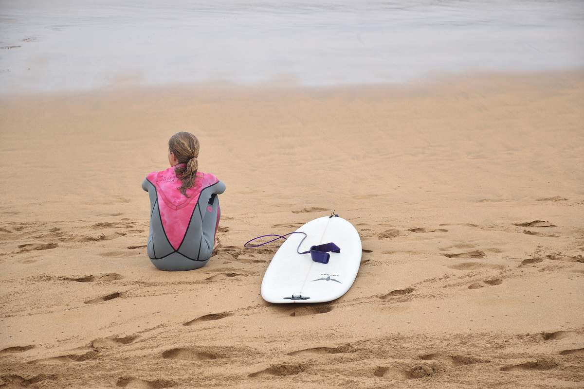 surfboard woman sitting on shore beside surfboard near sea sea