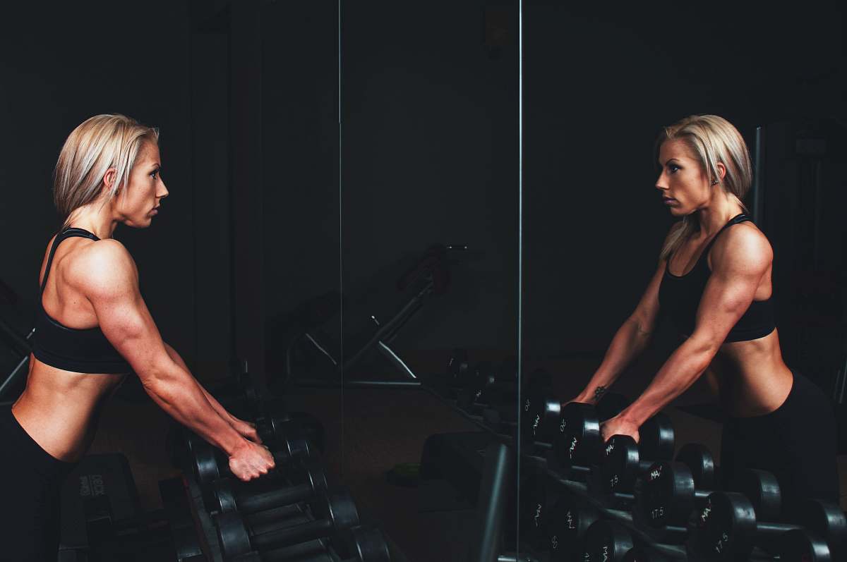 people woman wearing black top top holding black dumbbells standing in front of mirror fitness