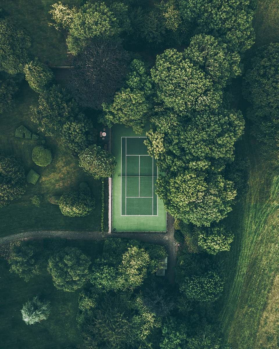 green aerial photo of tennis court surrounded with trees nature