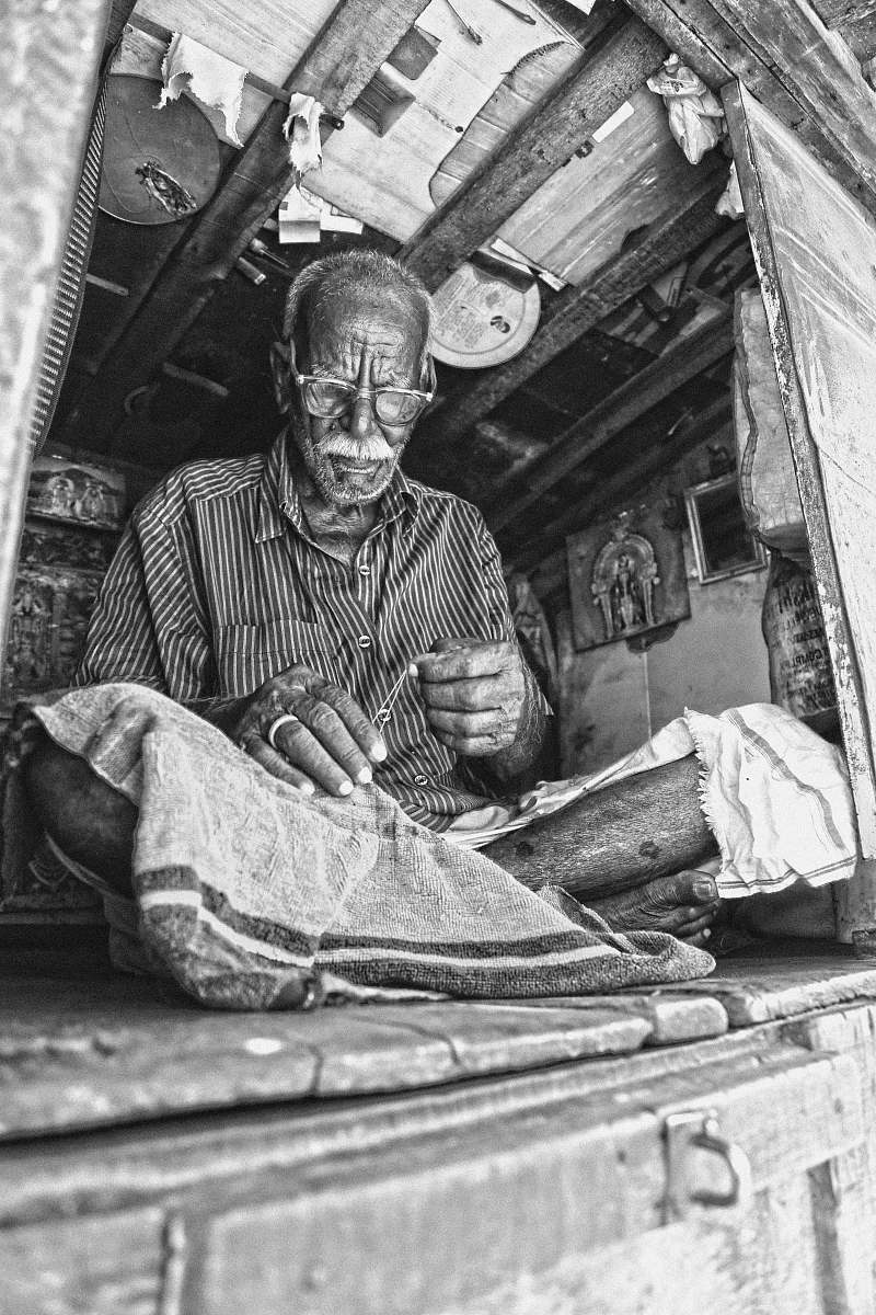 people grayscale photo of man sewing textile while sitting on floor india