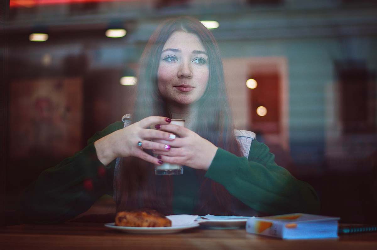person woman in green sweater sitting in front of table holding drinking glass people