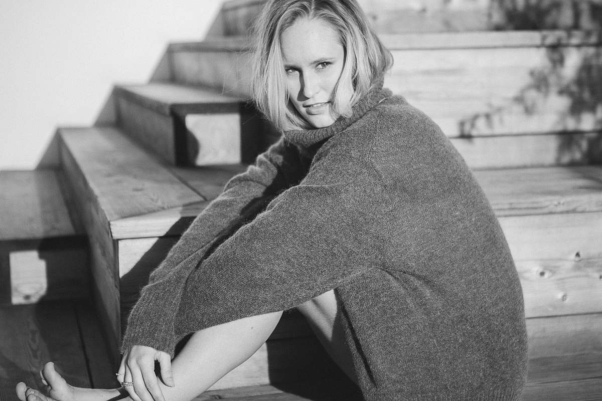person woman wearing cardigan sitting on stairs black-and-white