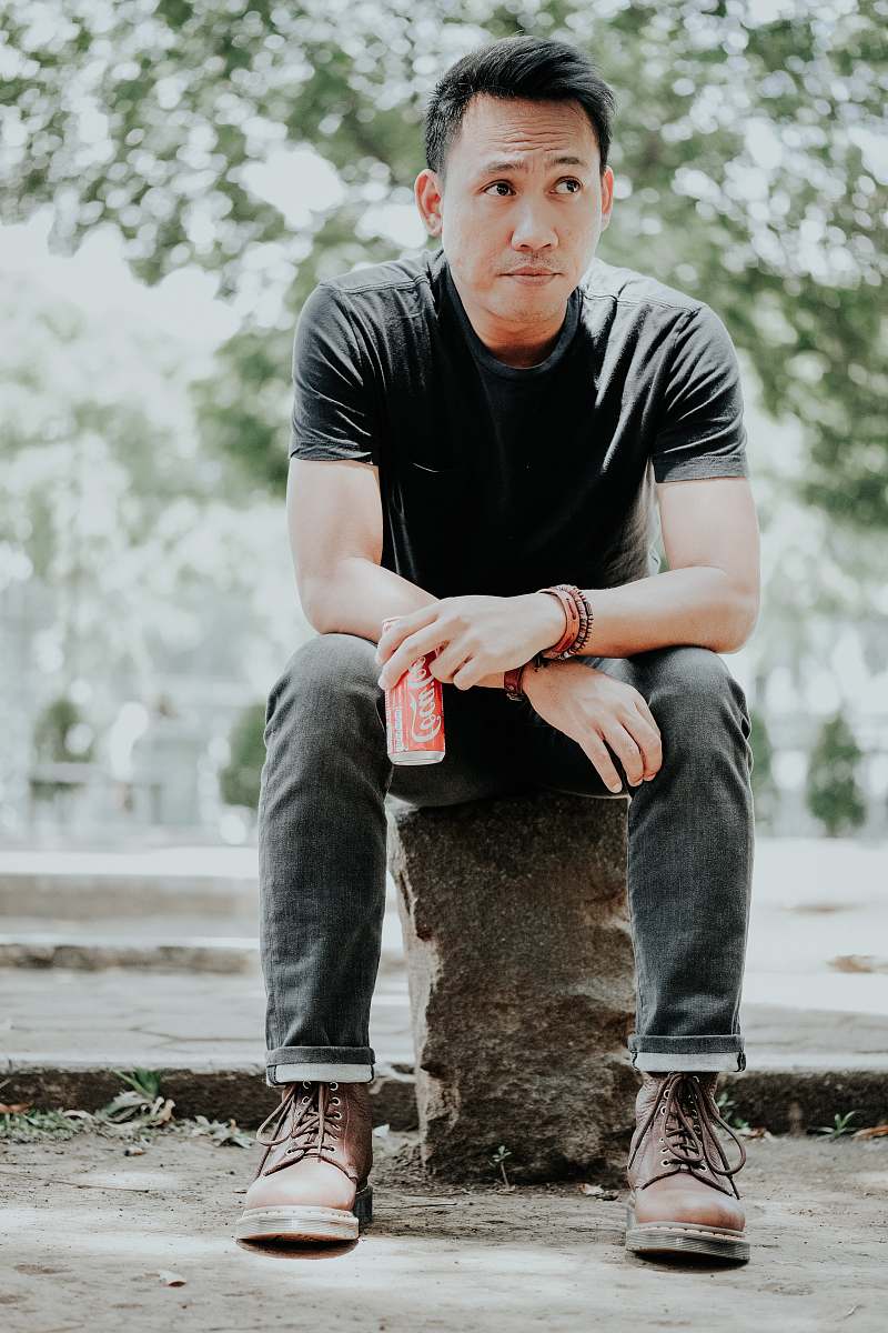 human man sitting on concrete while holding soda can person