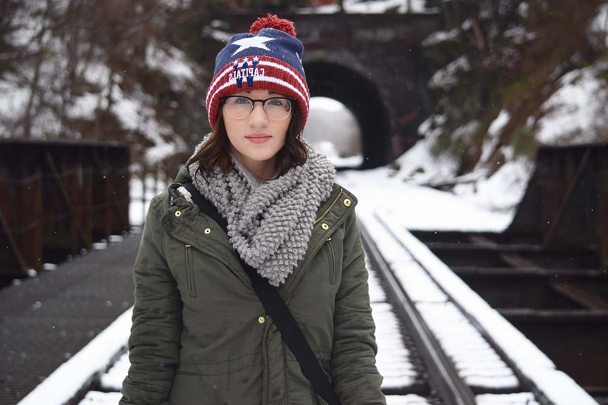 person woman in green coat carrying black sling bag standing on railway woman