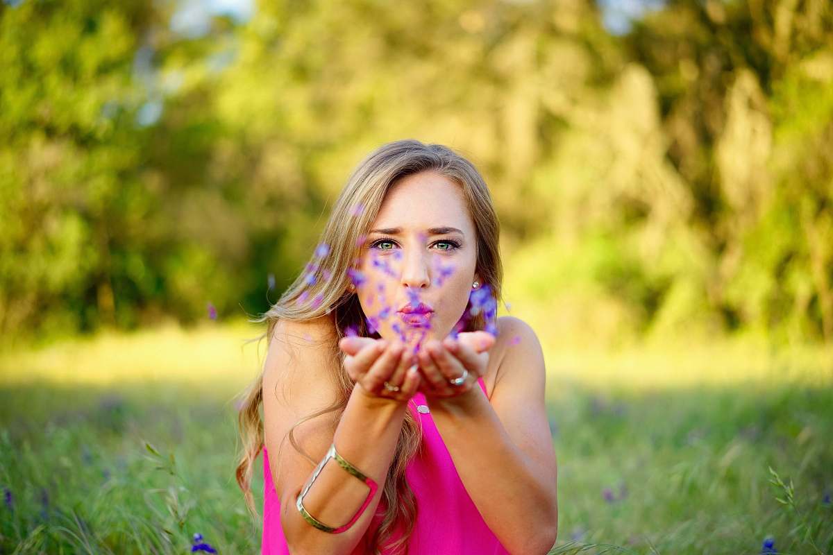 person woman wearing pink sleeveless top blowing purple flowers woman