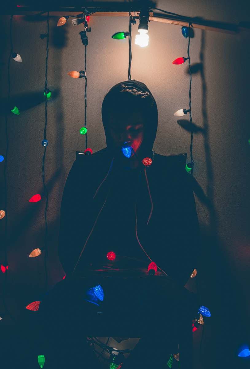 paper man sitting while biting multicolored string lights edinburg