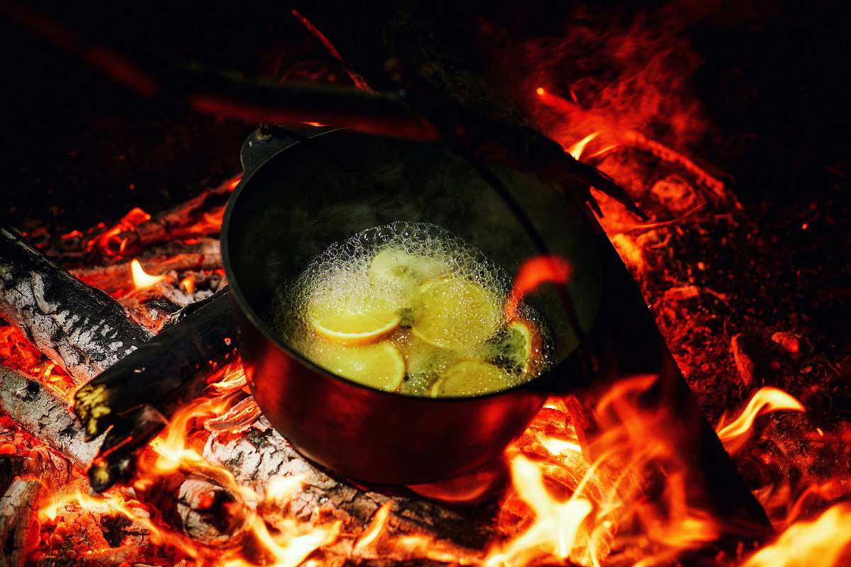 flame dutch oven on lit firewood with water and slices of fruits bonfire