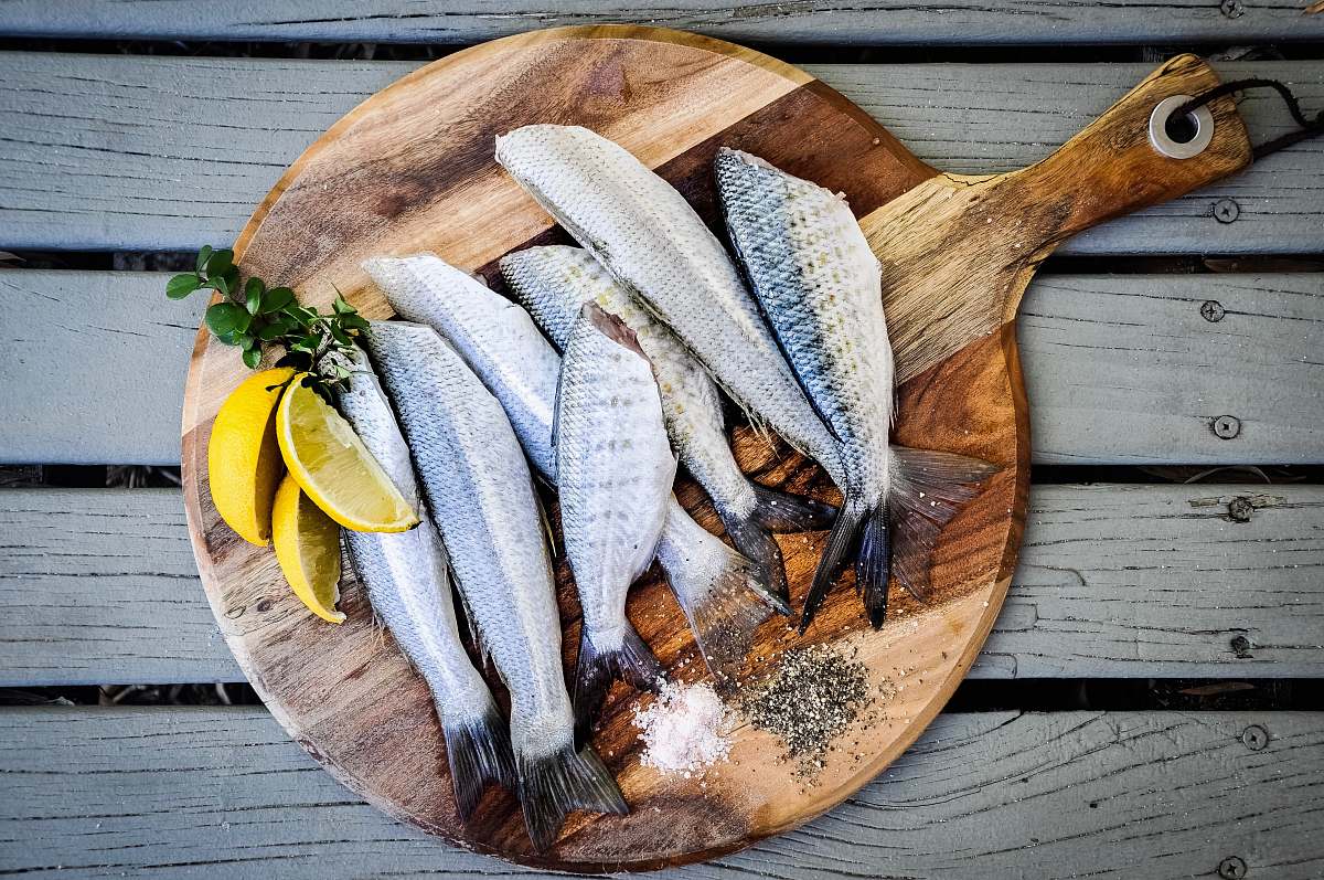 fish headless fishes with sliced of lemons on brown wooden chopping board chopping board