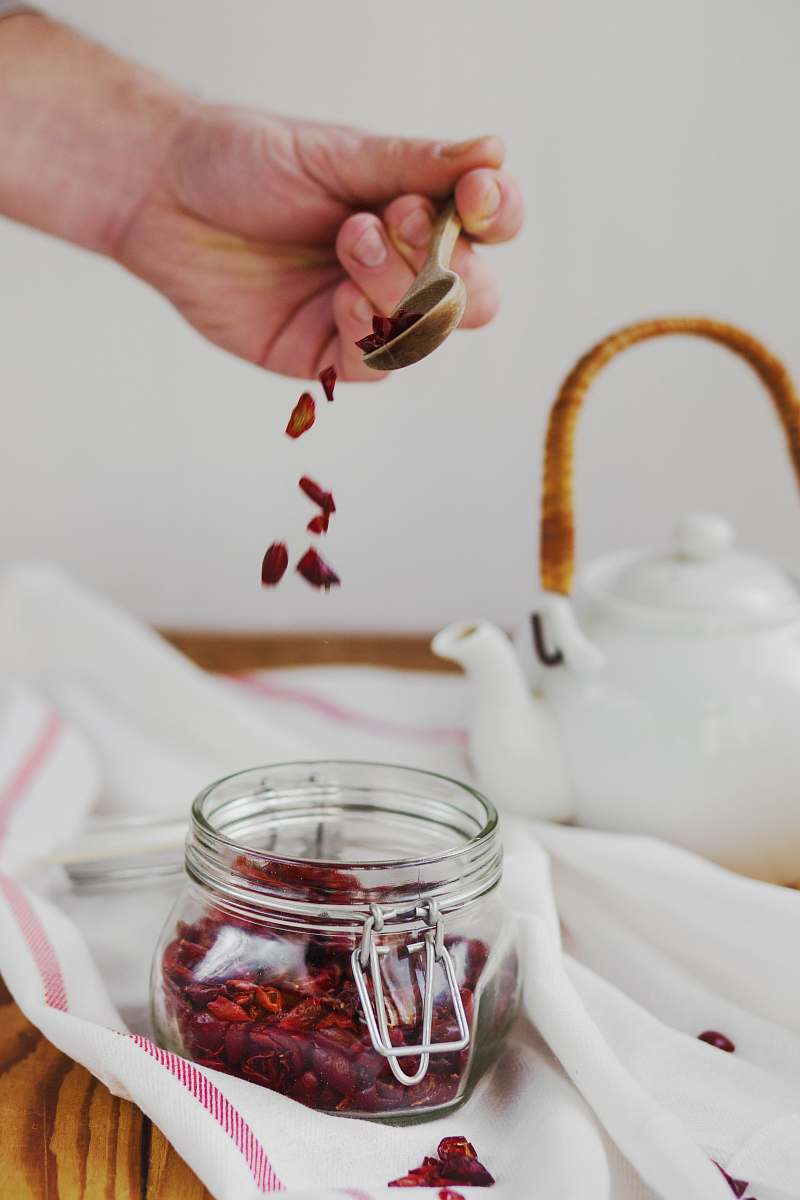 hands person holding brown spoon above clear glass jar holding