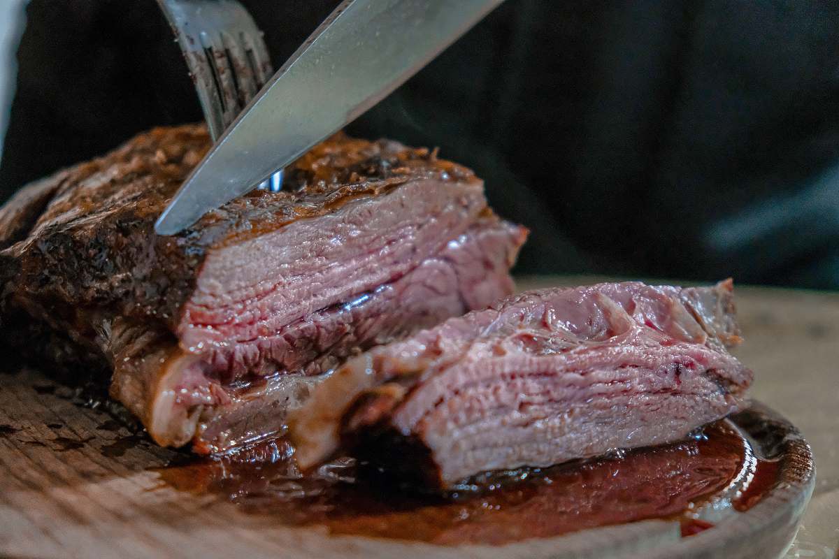 bbq person slicing juicy medium rare meat on top of brown wooden cutting board argentina