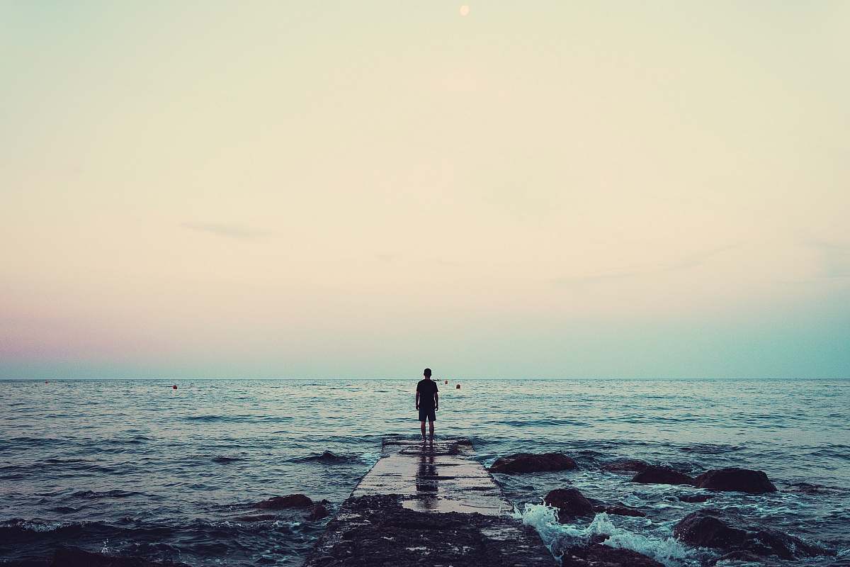 water silhouette of person standing on sea dock under cloudy sky ocean