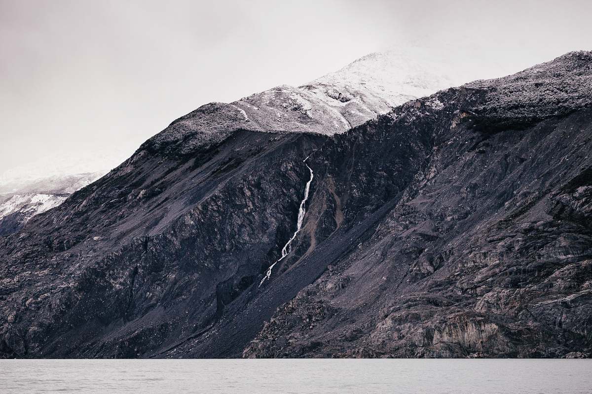 This breathtaking grayscale photograph captures the tranquil beauty of a body of water nestled amidst majestic mountains. The stillness of the water reflects the towering peaks, creating a stunning visual symmetry that is perfect for nature enthusiasts and landscape lovers. Ideal for use in travel magazines, environmental campaigns, or as a calming background for digital projects, this image conveys both serenity and grandeur.