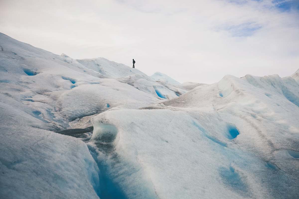 ice person standing on top of hill under white cloud blue skies glacier