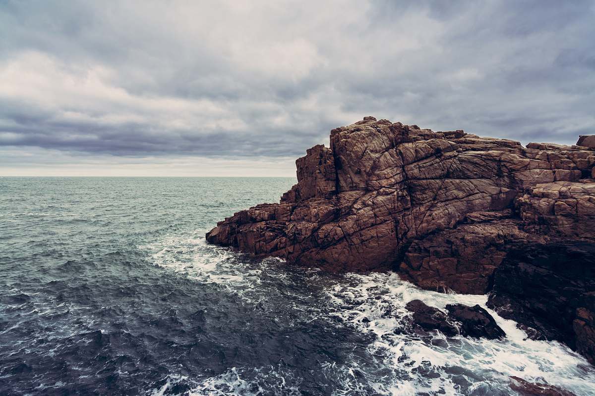 cliff photography of brown rock near body of water during daytime clouds