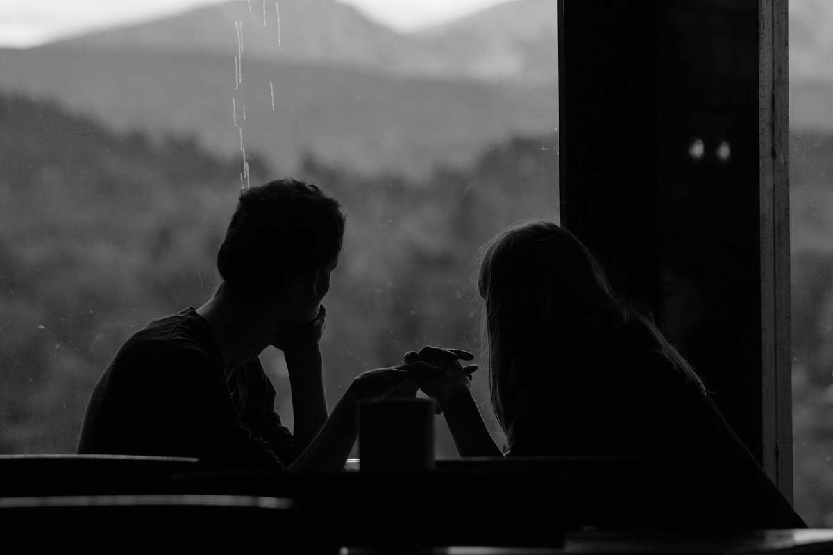 human grayscale photography of couple sits by the window black-and-white