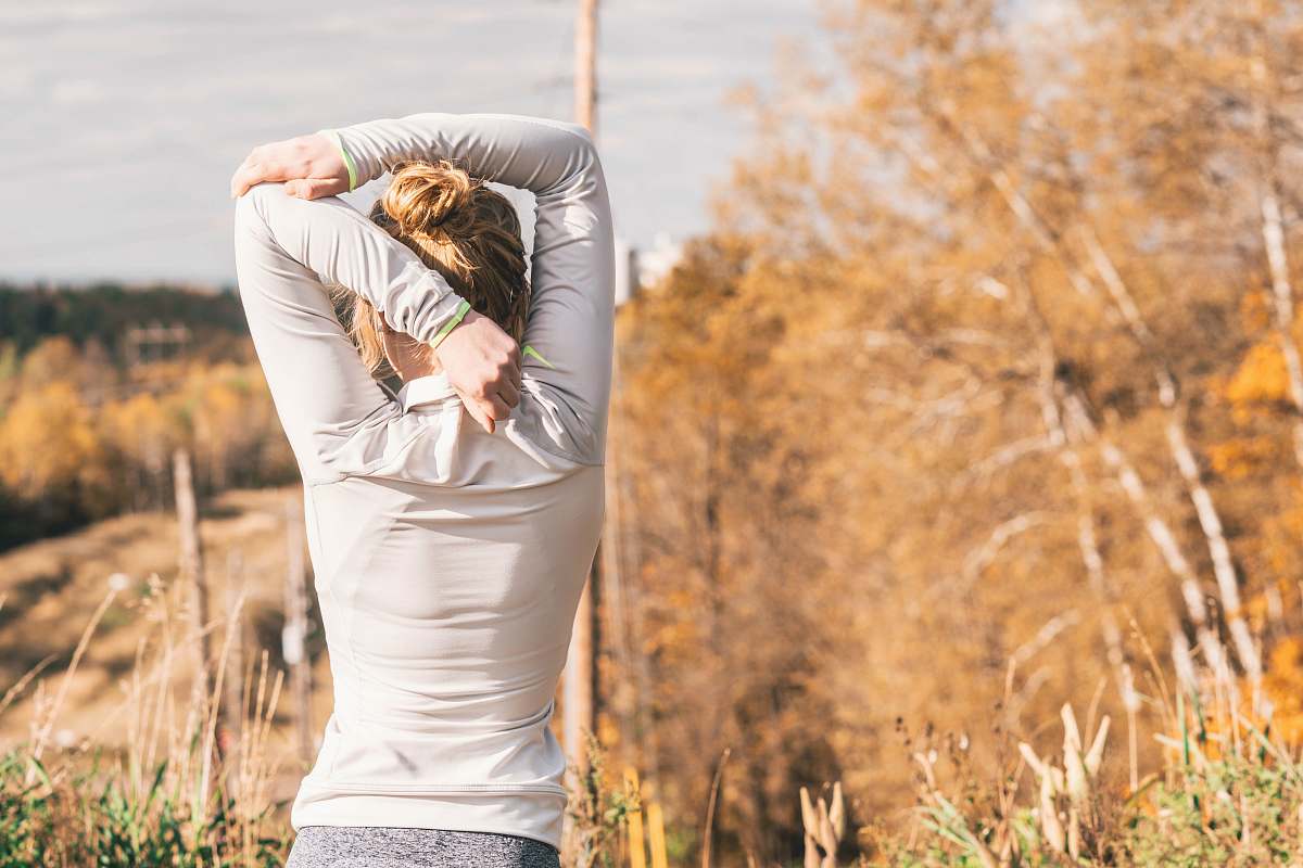 human woman standing while stretching beside brown leafed trees people