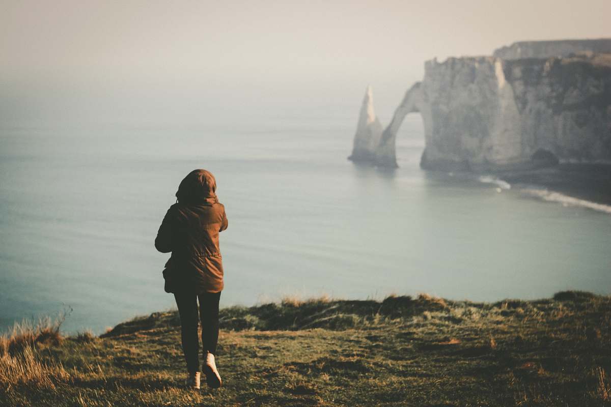 nature woman walking towards the edge of island facing the ocean during day fog