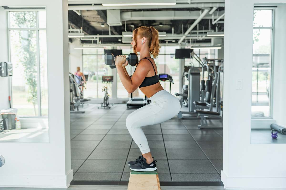human woman wearing black sports bra and white legging lifting dummbells sports