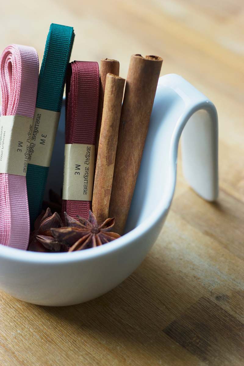 wood star anise, cinnamon roll, and several garters on round white ceramic bowl on top of brown surface ribbon