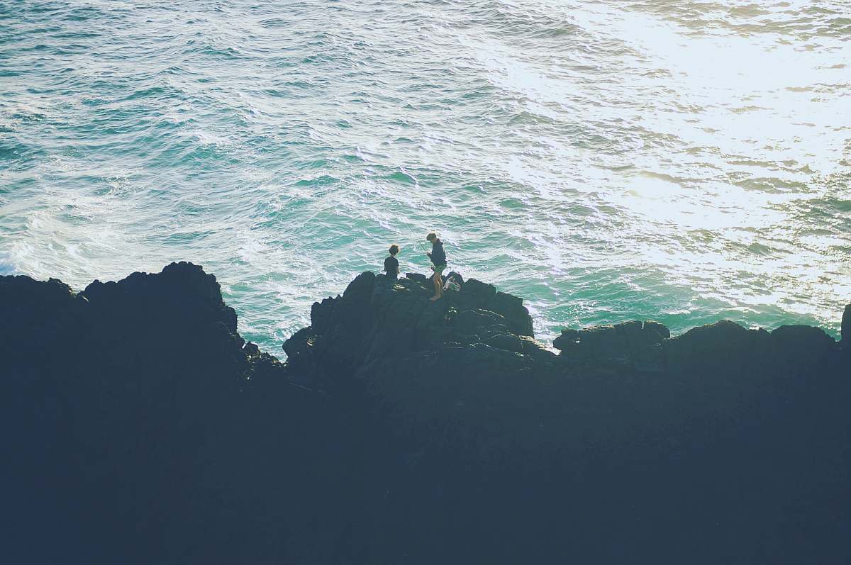 sea two person standing on the cliff near the ocean rocks