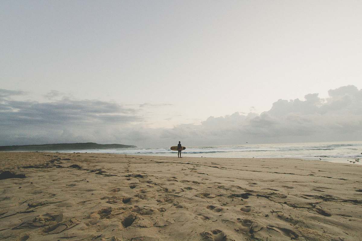 surfer man standing by the seashore with surfboard sand