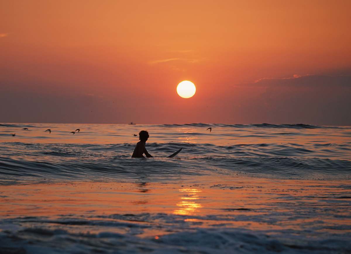 nature silhouette photo of person riding a surfboard surf